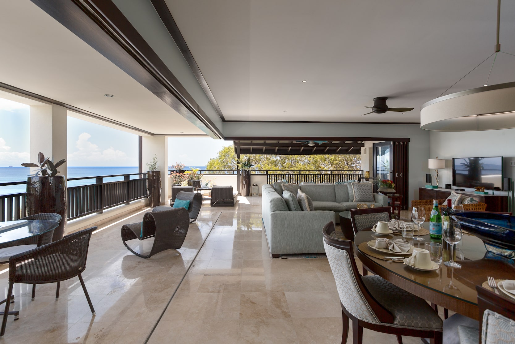 Spacious, modern open-plan living and dining area with large windows, light marble floors, and a balcony overlooking the ocean and greenery under a sunny sky—welcome to Crowsnest – Coral Cove 14.